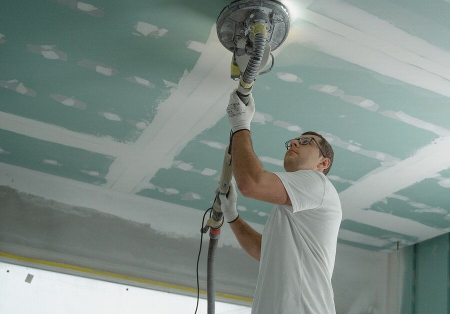 Worker sanding a ceiling with a pole sander in a room under renovation