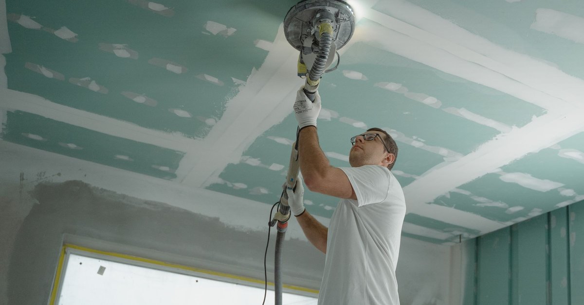 Worker sanding a ceiling with a pole sander in a room under renovation